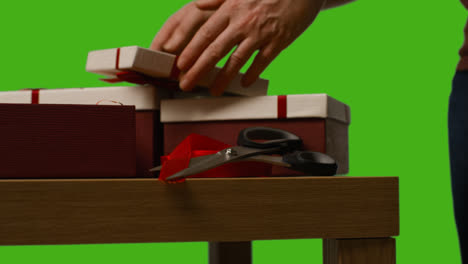 Close-Up-Of-Man-Gift-Wrapping-Presents-In-Boxes-Decorated-With-Ribbon-On-Table-Shot-Against-Green-Screen-3